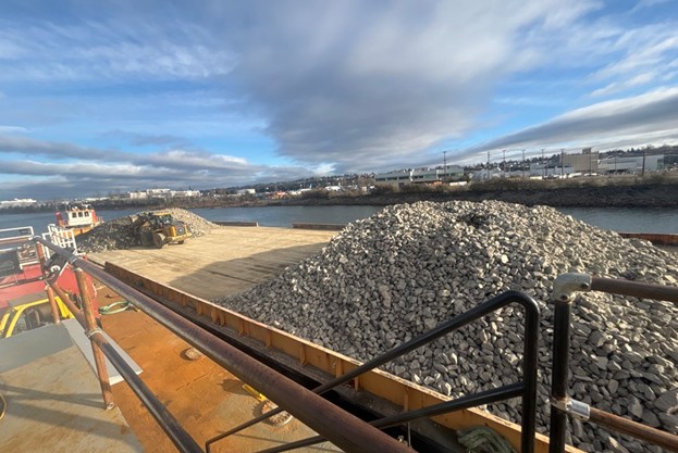 Photo of barge on waterway with two piles of large, clean rock.